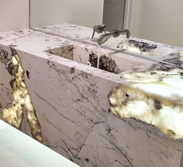 Back-lit alabaster stone bathroom vanity glowing warmly with a wall-mounted faucet.