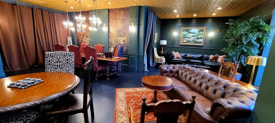 Moody entertainment lounge with a tufted leather chesterfield sofa, red accent chairs and a games table.