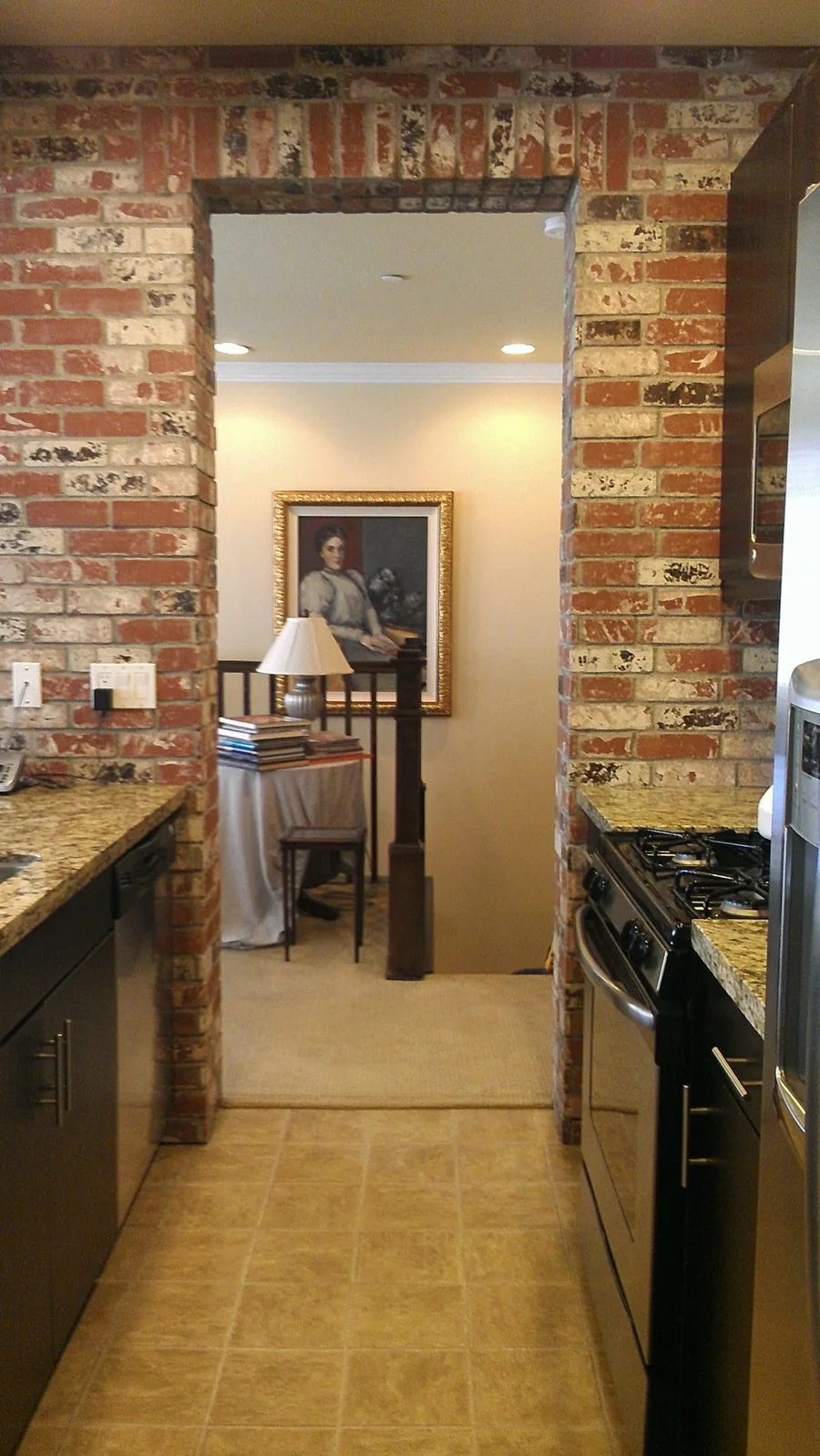 Galley kitchen viewed through a reclaimed brick archway with granite counters.