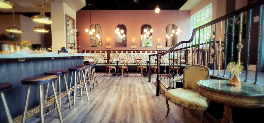 Interior of Corbeaux café in Temecula with a dark bar counter, warm wood floors, bar stools and vintage seating.