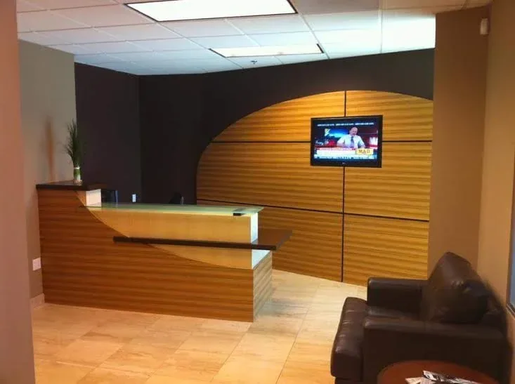 Office reception area with a curved wood desk, wall-mounted display and lounge seating.