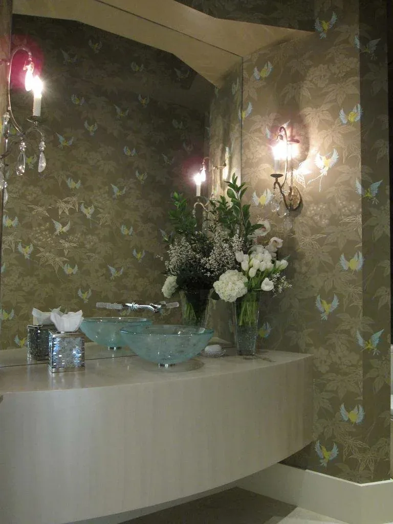 Powder room with a glass vessel sink, botanical wallpaper, candle sconces and a fresh floral arrangement.