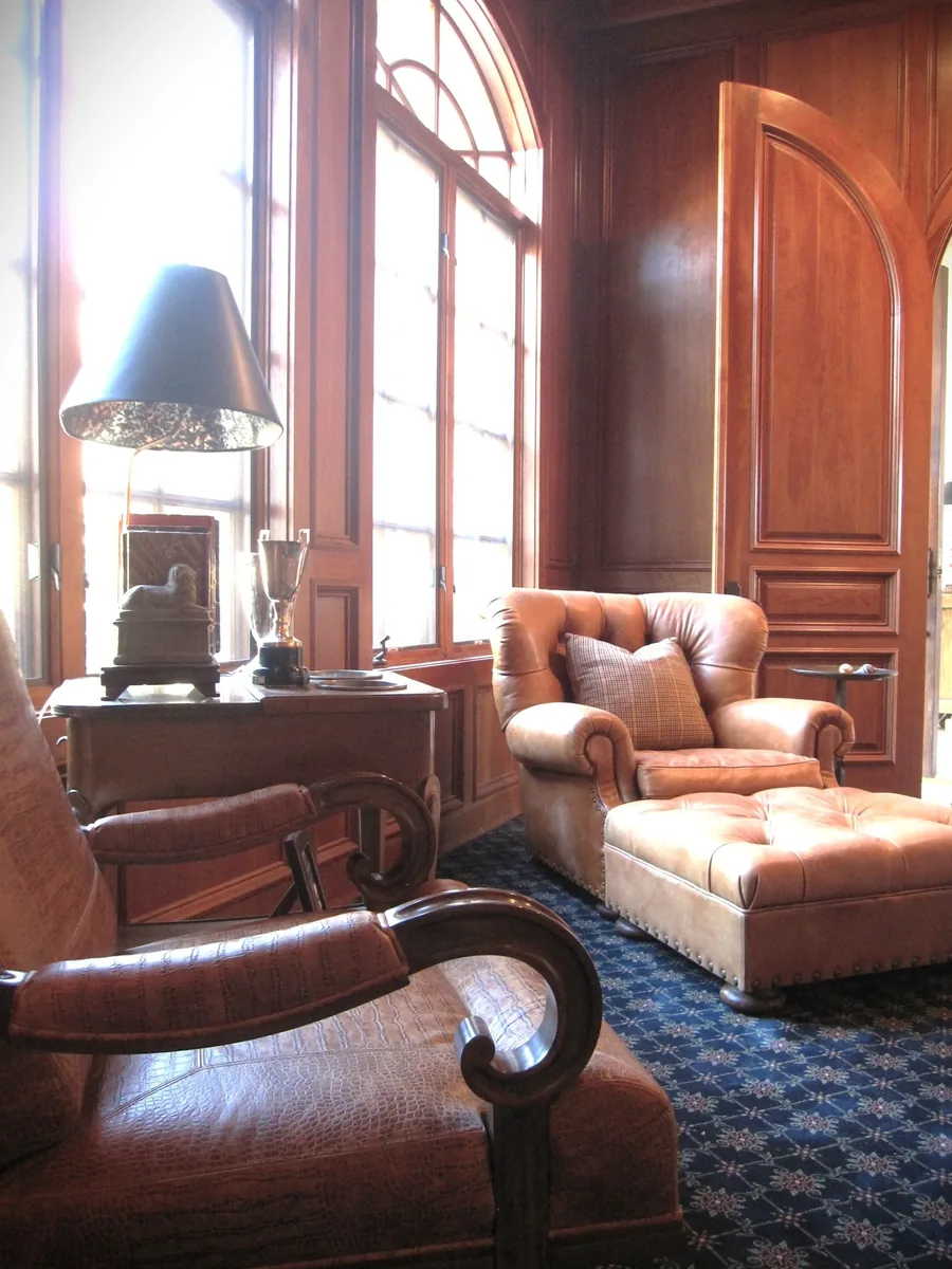 Richly paneled study with leather club chairs, an arched window and a warm reading lamp.