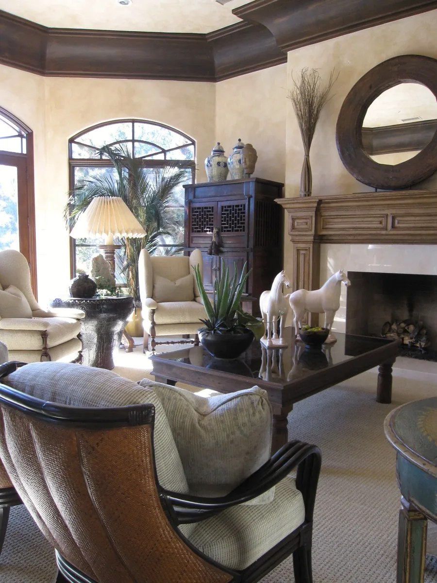 Mediterranean living room with a carved stone fireplace, round mirror, palms and sculptural accents.