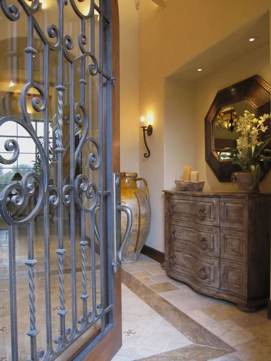 Entry hall framed by a decorative wrought-iron screen with a carved chest and mirror.