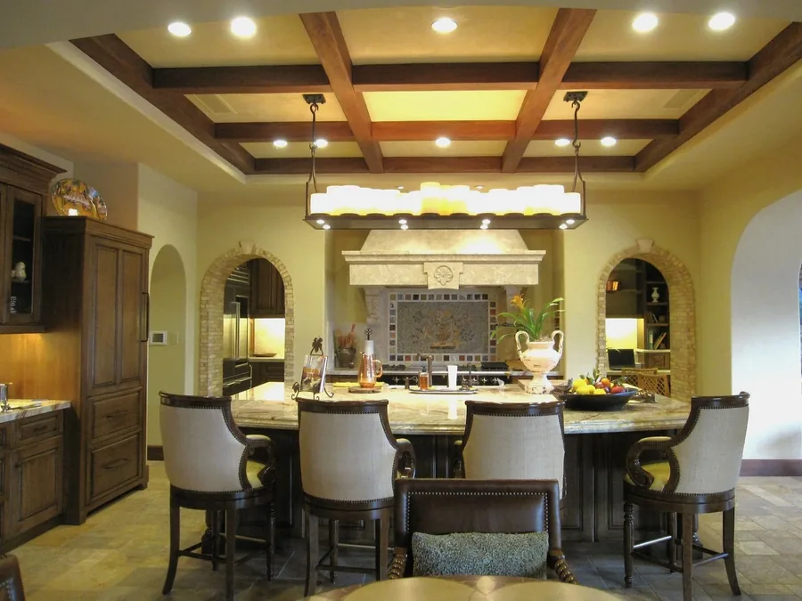 Formal dining room with a coffered wood ceiling, linear chandelier, arched niches and upholstered chairs.