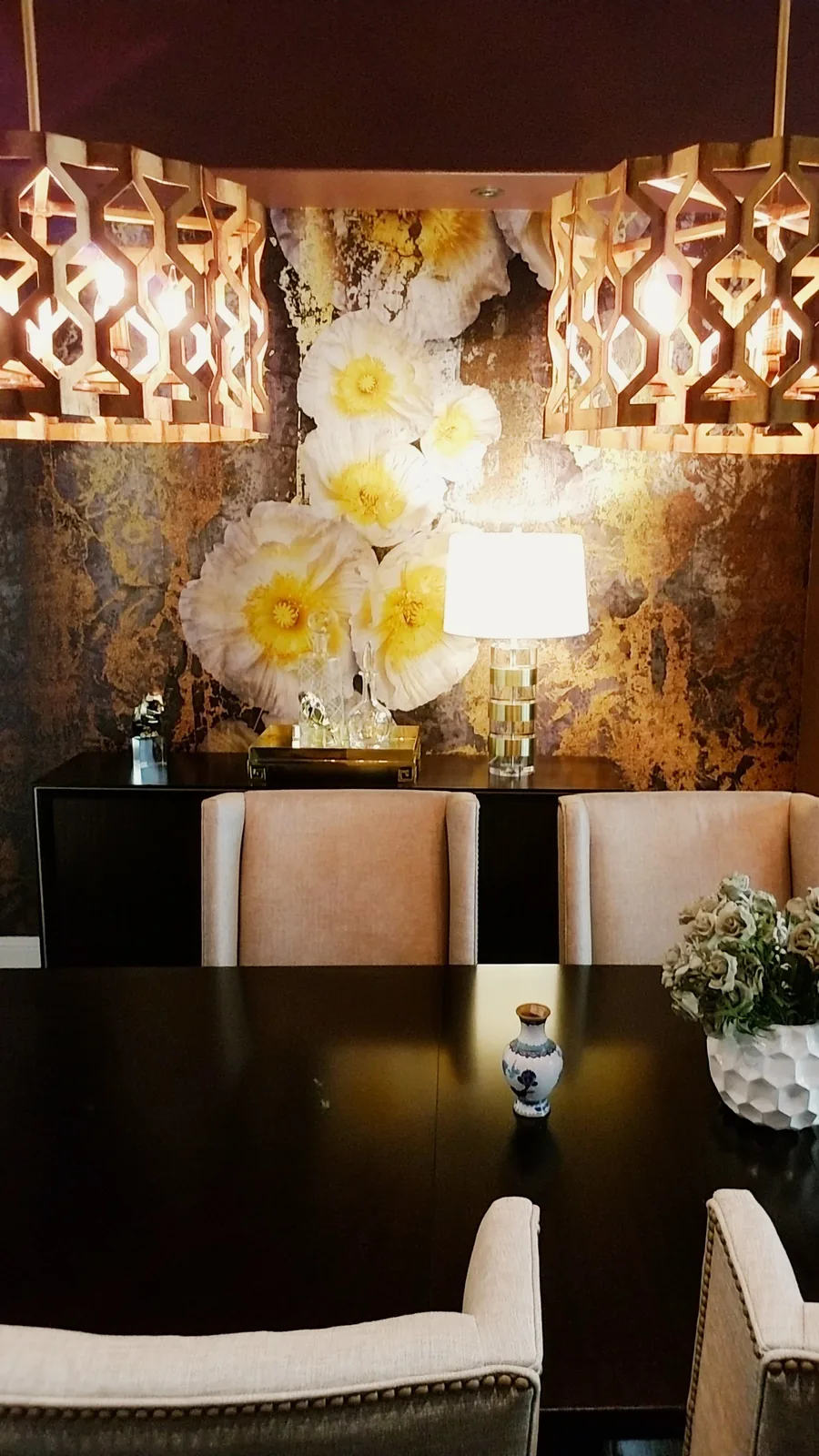 Dining vignette with a textured metallic-gold floral wall, sculptural florals and upholstered chairs.