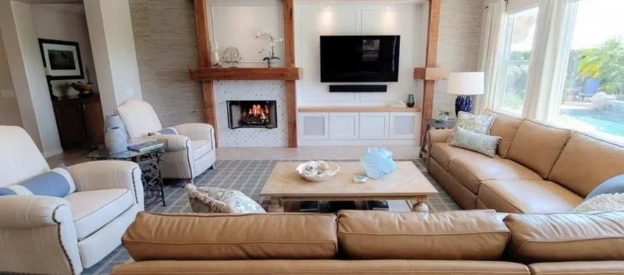 Family room with a tan leather sectional, fireplace, television and warm natural light.