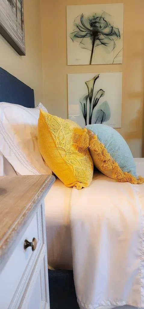 Guest bedroom in crisp white with citrine-yellow and teal pillows and botanical prints.