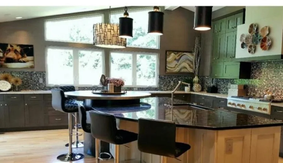 Kitchen with sage-green cabinet accents, a mosaic backsplash, black bar stools and pendant lighting.