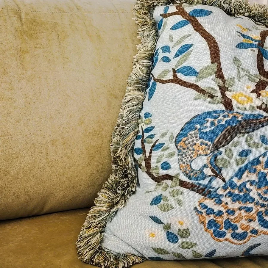 Textile detail of a peacock-embroidered pillow against a soft gold cushion.