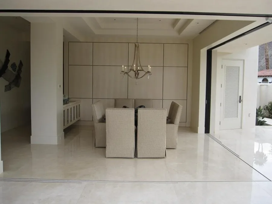 Minimalist pale dining and living space with marble floors and a modern chandelier.