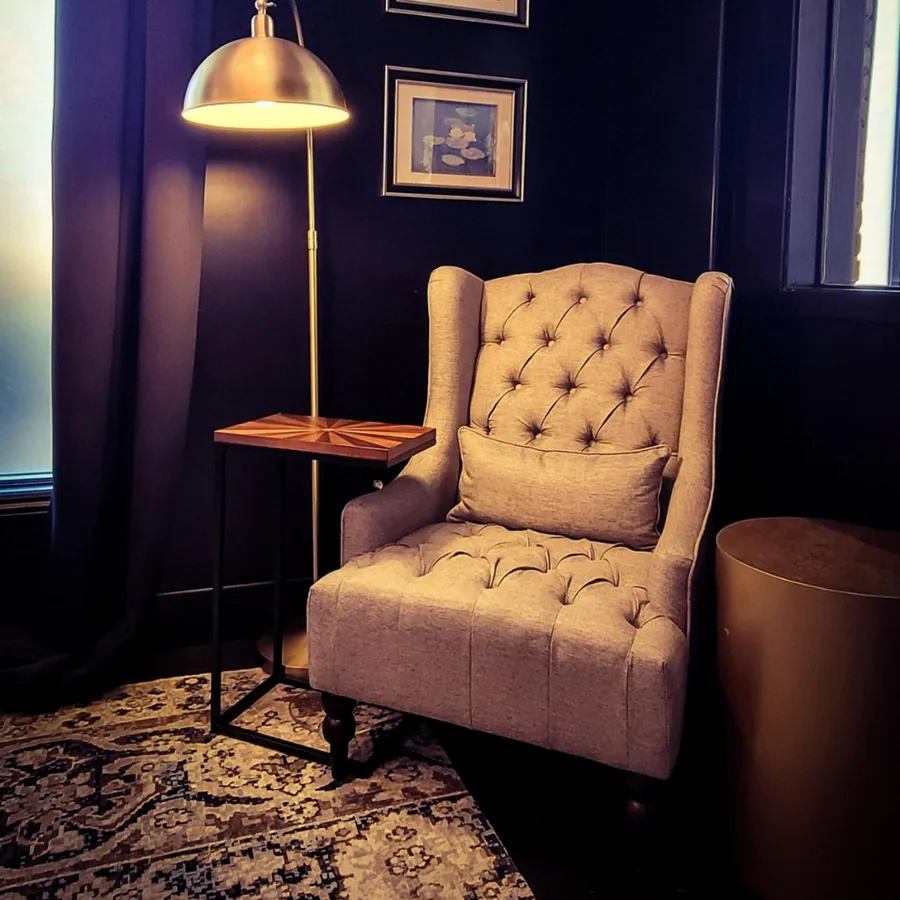 Intimate study nook with plum walls, a tufted wing chair, brass floor lamp and patterned rug.