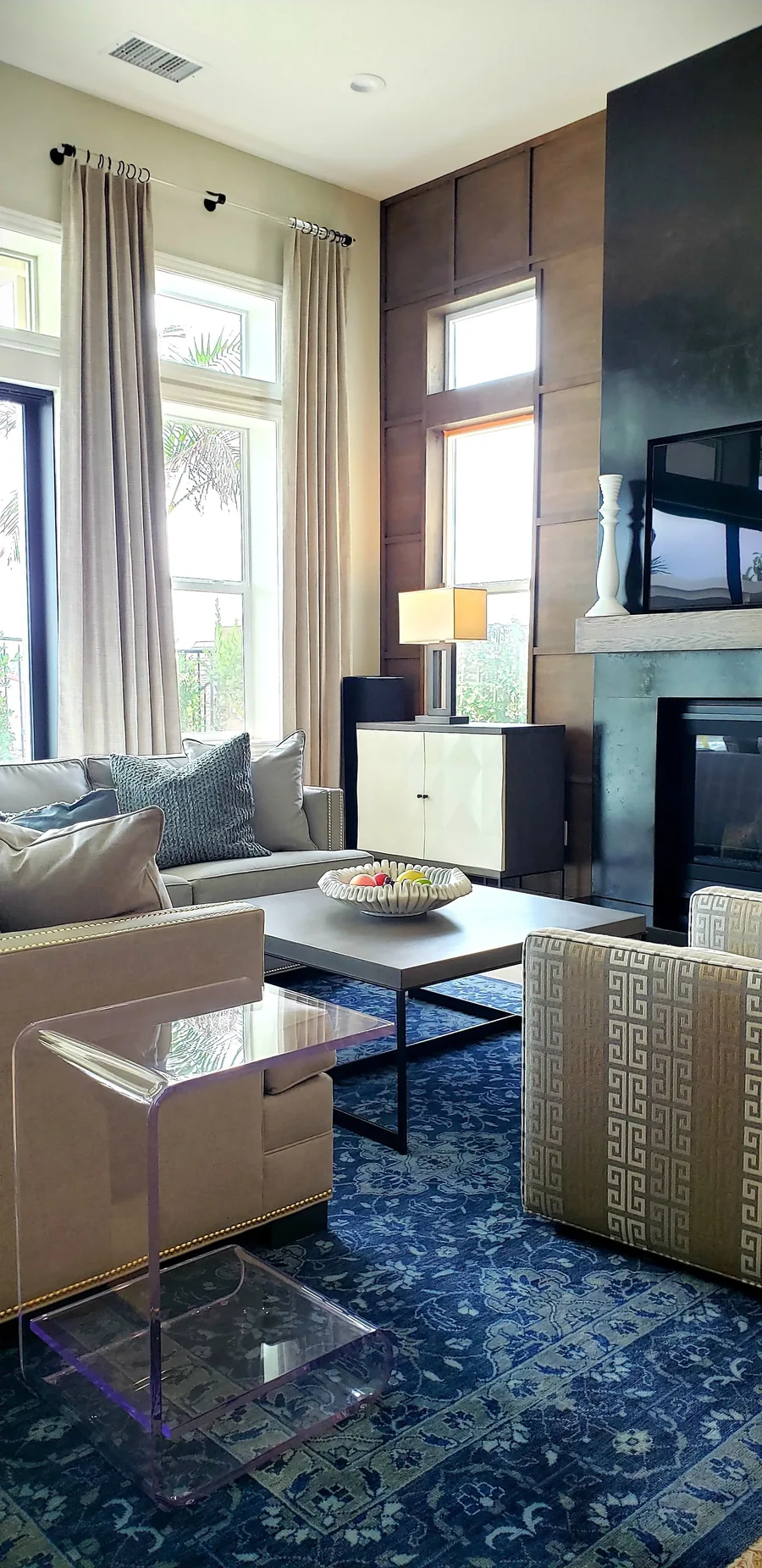 Living room with neutral seating, a sapphire-blue patterned rug, fireplace and glass coffee table.