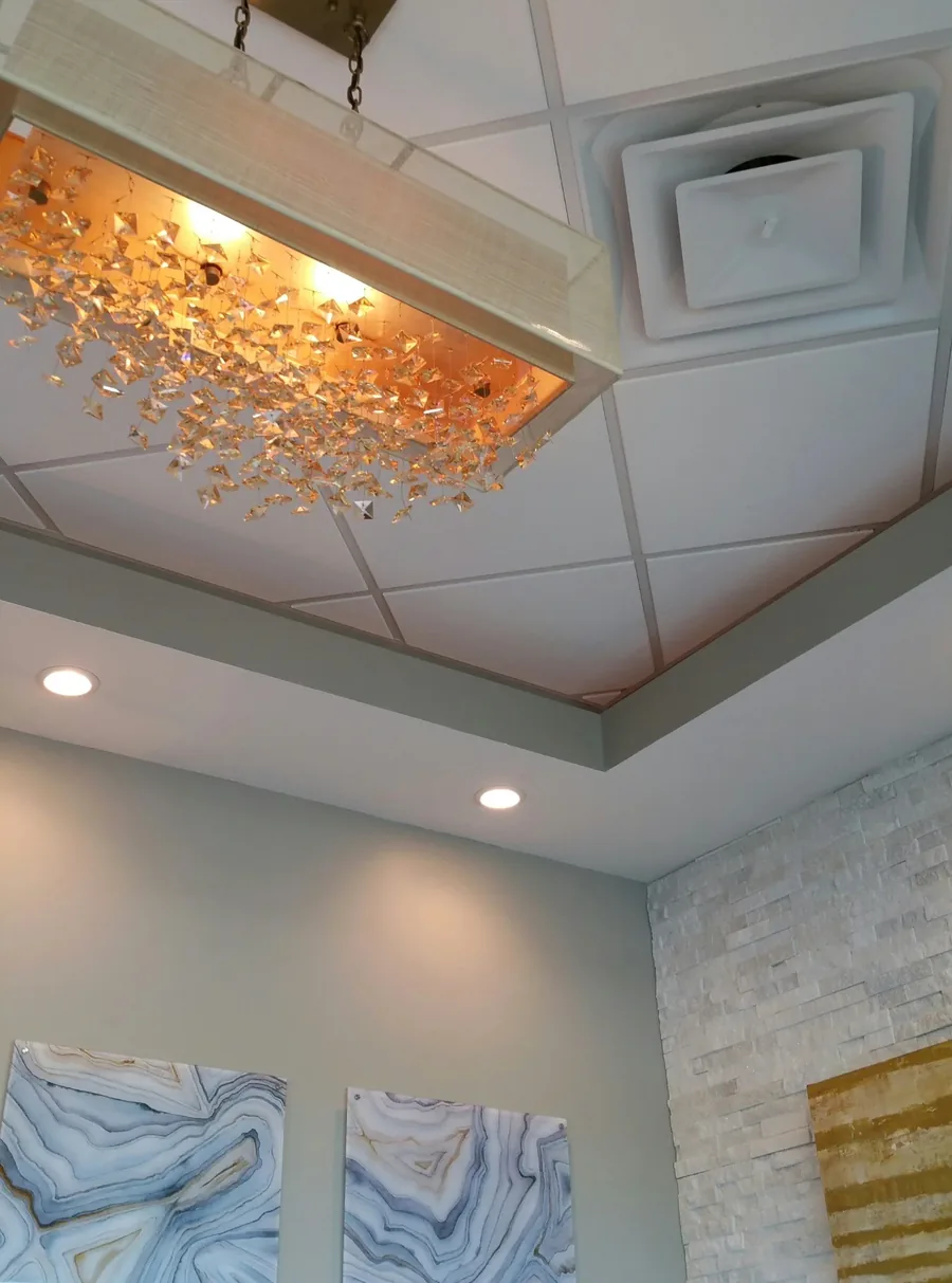 Coffered tray ceiling with a dramatic gilded branch chandelier above a stone accent wall.