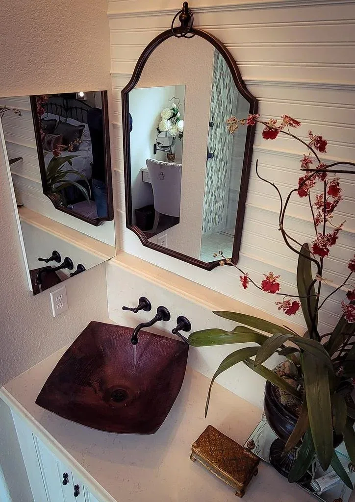 Powder room with a carved dark-red vessel sink, ornate mirror, plank wall and orchids.