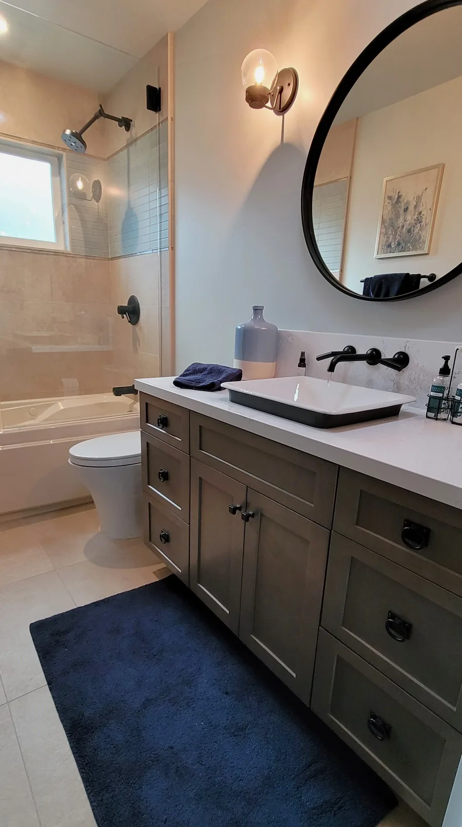 Modern bathroom with a dark wood vanity, round mirror, black fixtures and a glass walk-in shower.