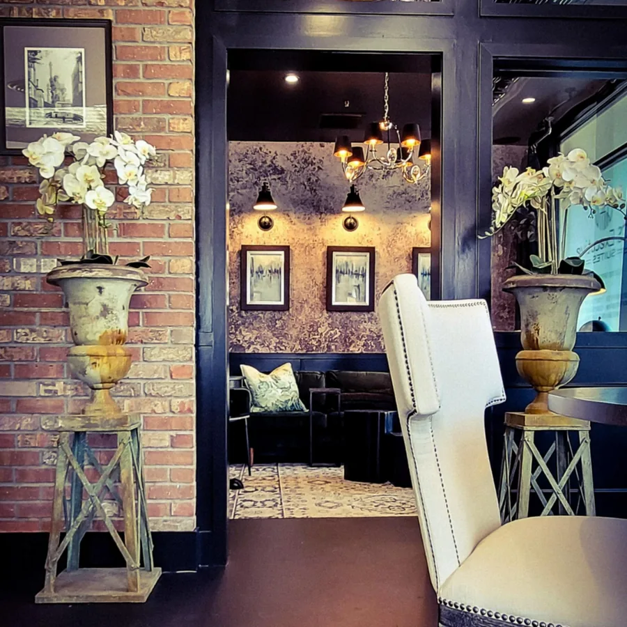 Lounge with exposed brick, plum walls, tall urns with orchids and pairs of upholstered chairs.