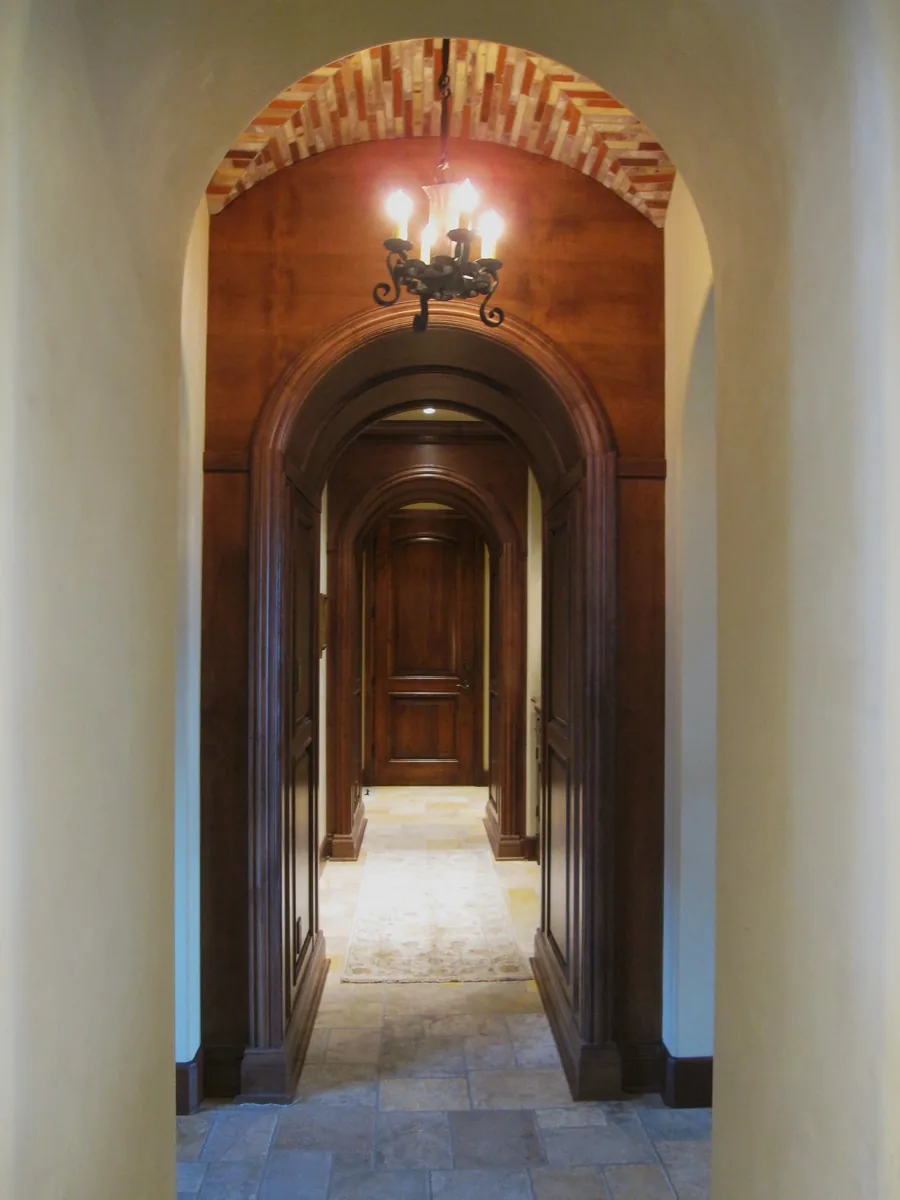Architectural entry with a barrel brick ceiling arch and a carved wood door beyond.